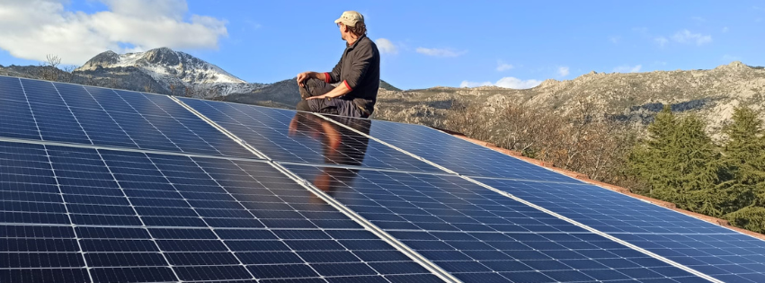 Banner web solar fotovoltaica placas solares en tejado con persona subida encima y montañas del fondo