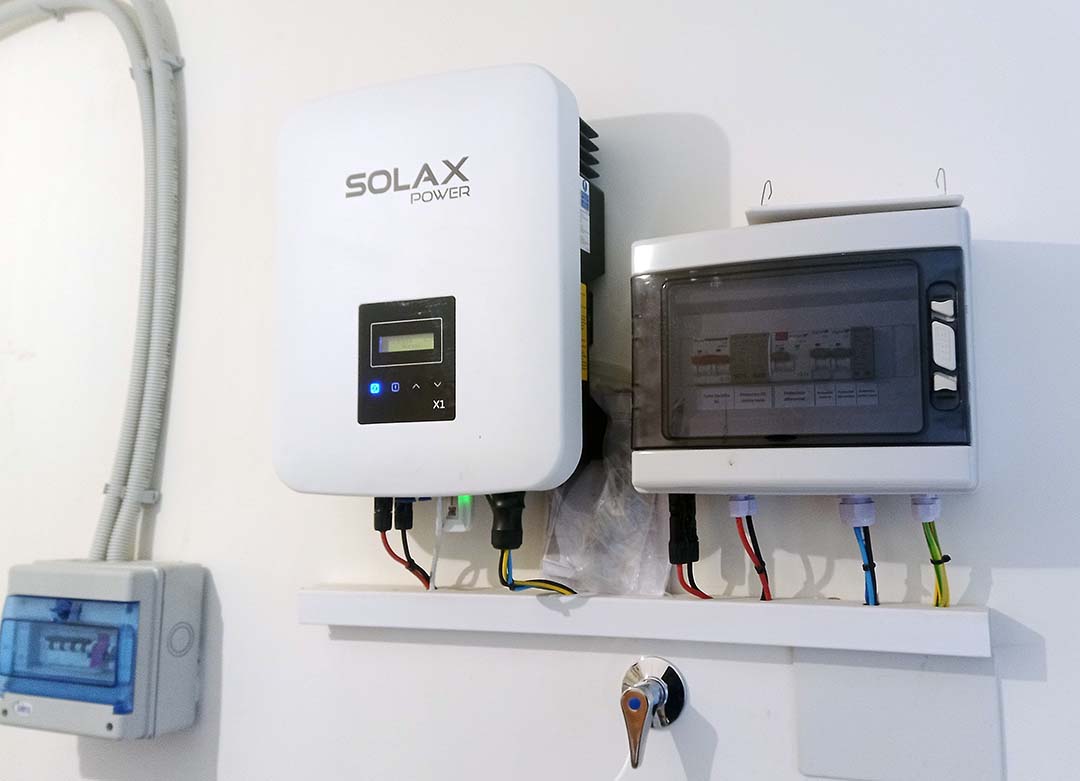 dos cajas una blanca y otra con tapa oscura transparentes que son máquinas que permiten la generación de energía con paneles solares. Están colgadas de una pared blanca